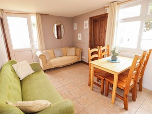 A room with a green sofa, a beige sofa, a wooden dining table with chairs, a wooden door, and a window with curtains. - Chalet 242 Carmarthen Bay (Kidwelly)