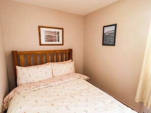 A bedroom with a bed, a wooden headboard, and two framed pictures on the wall. - Chalet 242 Carmarthen Bay (Kidwelly)
