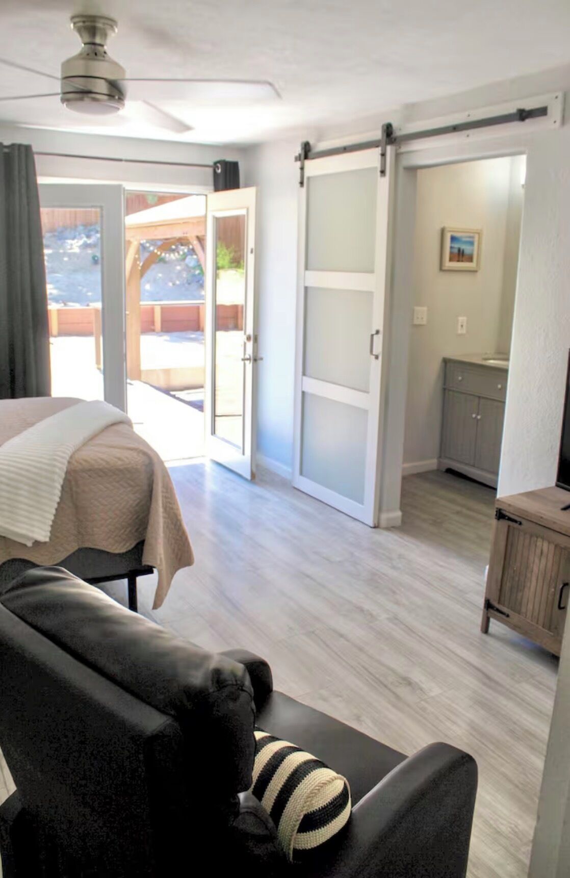A room with a bed, a sofa, a sliding door leading to an outdoor area, and a small kitchenette.