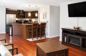 A modern kitchen with wooden cabinets, a central island with chairs, a built-in stove, and a flat-screen TV mounted on the wall. - Modern Reno Retreat -Near UNR & Downtown - Sleeps 10 (Reno)