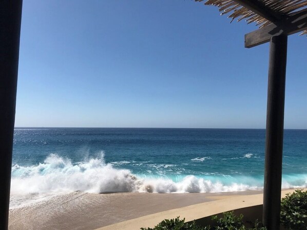 Une vue sur la plage, avec des vagues qui déferlent sur le rivage, un ciel dégagé et une construction surmontée d’un toit de chaume.