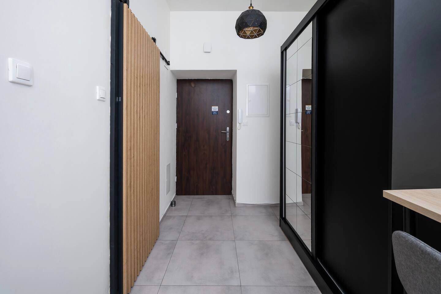 A hallway with a wooden panel wall, a door, and a black-framed glass door.