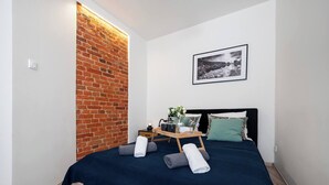 A modern bedroom with a brick accent wall, a neatly made bed with pillows and a tray of toiletries, and a framed picture on the wall. - Łódź Płocka Apt – Parks & Public Transport nearby (Łódź)