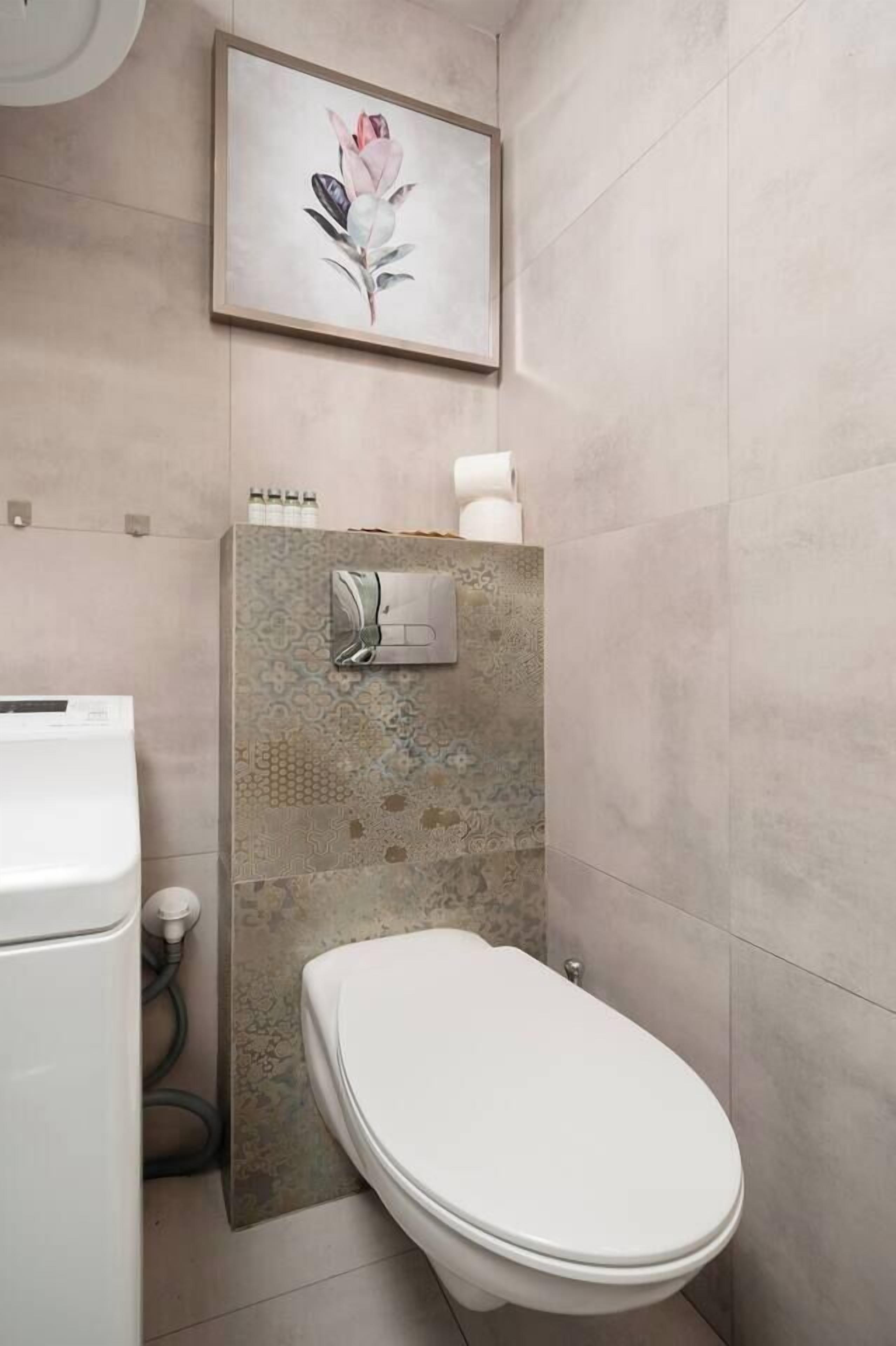 Ein modernes Badezimmer mit Toilette, einem Wand-Toilettenpapierhalter und einem gerahmten Blumenbild über der Toilette.