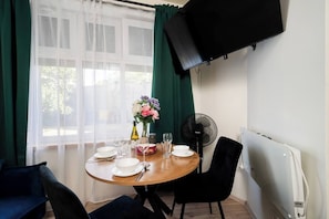 En matplats med ett bord dukat för två personer, en vas med blommor, en fläkt och en tv som är monterad på väggen.