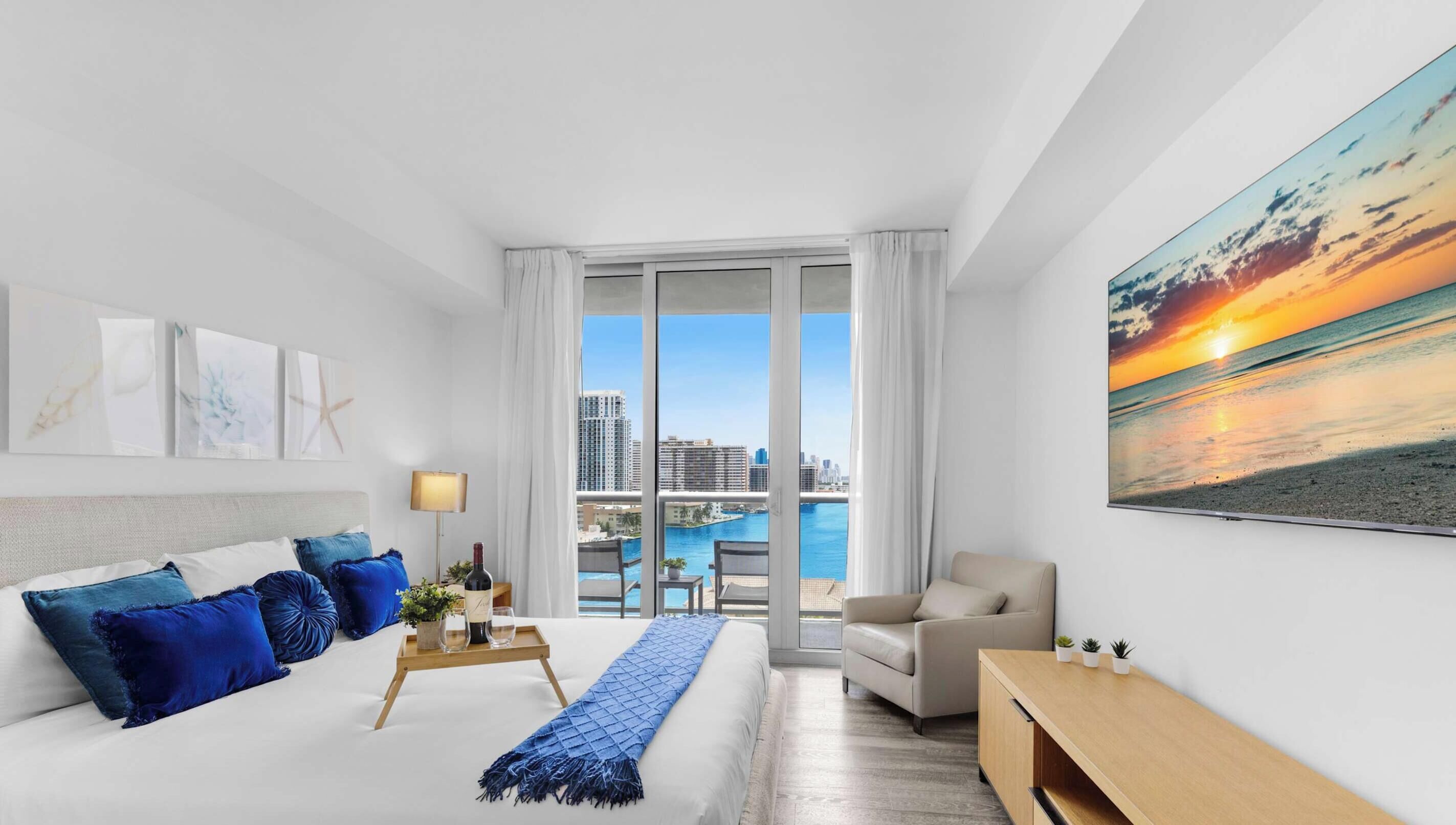 A modern hotel room with a large bed, a desk, a chair, and a view of the city and water.