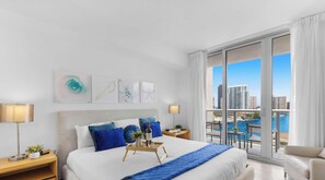 Habitación de hotel moderna con una cama grande, vistas a la ciudad y un balcón con piscina.