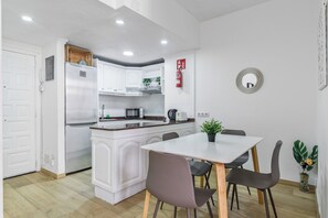 A compact kitchen with white cabinetry, a built-in microwave, and a small dining area with a table and chairs. - Home2Book Las Canteras Beach & City Stay (Las Palmas de Gran Canaria)