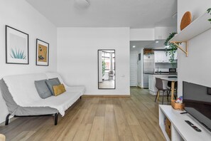 A modern living room with a white sofa, a flat-screen TV, and a kitchen area visible through an open door. - Home2Book Las Canteras Beach & City Stay (Las Palmas de Gran Canaria)