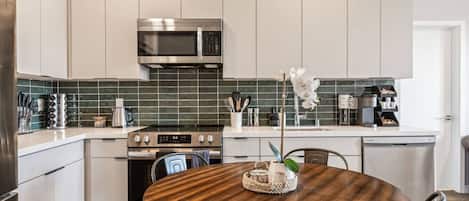 A modern kitchen with white cabinetry, a stainless steel microwave, and a round wooden dining table with chairs.