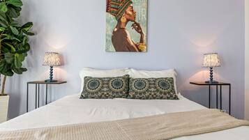 A bedroom with a bed, two nightstands, two lamps, a large poster, and a potted plant.