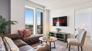Ett modernt vardagsrum med en stor platt-TV, bekväma sittplatser och utsikt över stadsbilden.