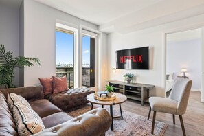A modern living room with a large flat-screen TV, comfortable seating, and a view of the cityscape.