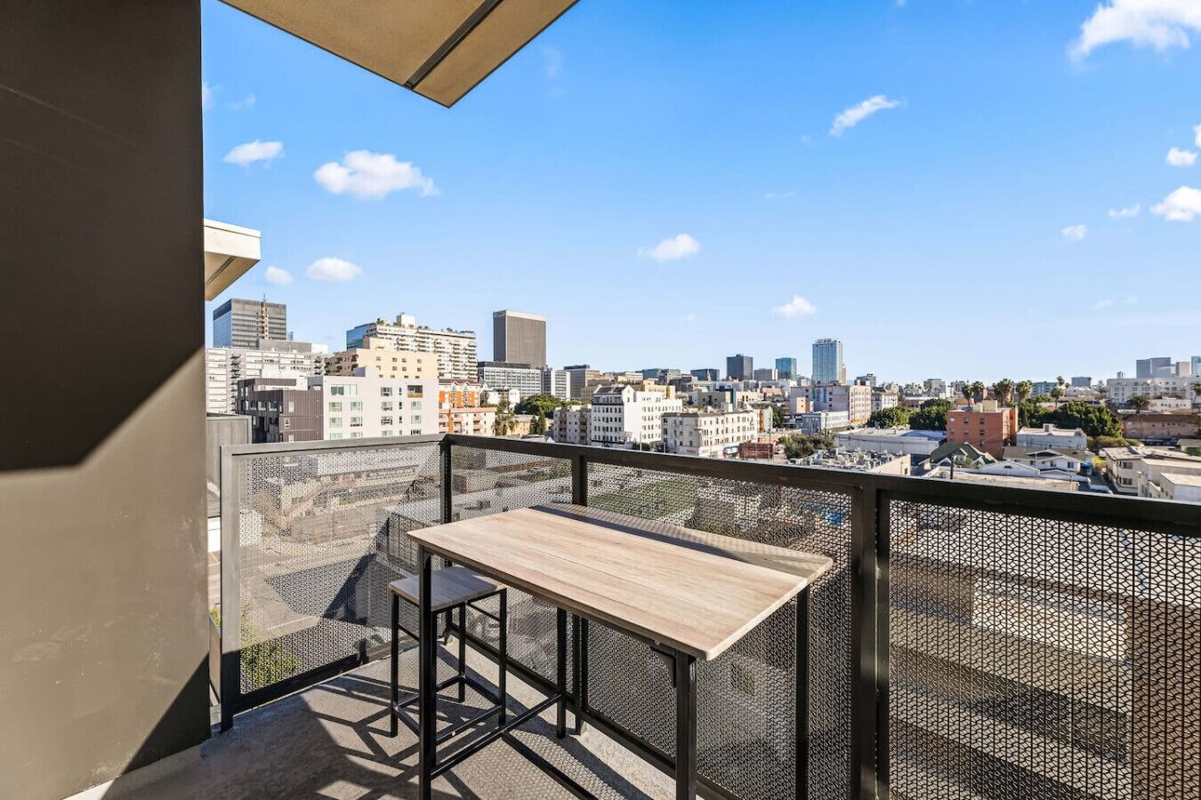 A balcony with a table and chairs, overlooking a cityscape with various buildings.