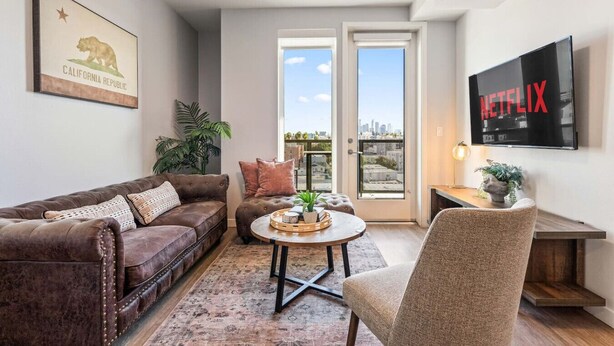 Uma sala de estar com sofá de couro marrom, mesa de centro redonda e televisão exibindo 'NETFLIX'.