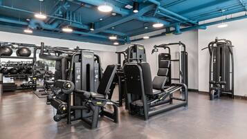 Ett gym med olika träningsmaskiner, en vägg täckt med speglar och ett tak med synliga rör.