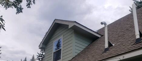 A two-story house with a gabled roof, a chimney, and a window with a view of a tree.