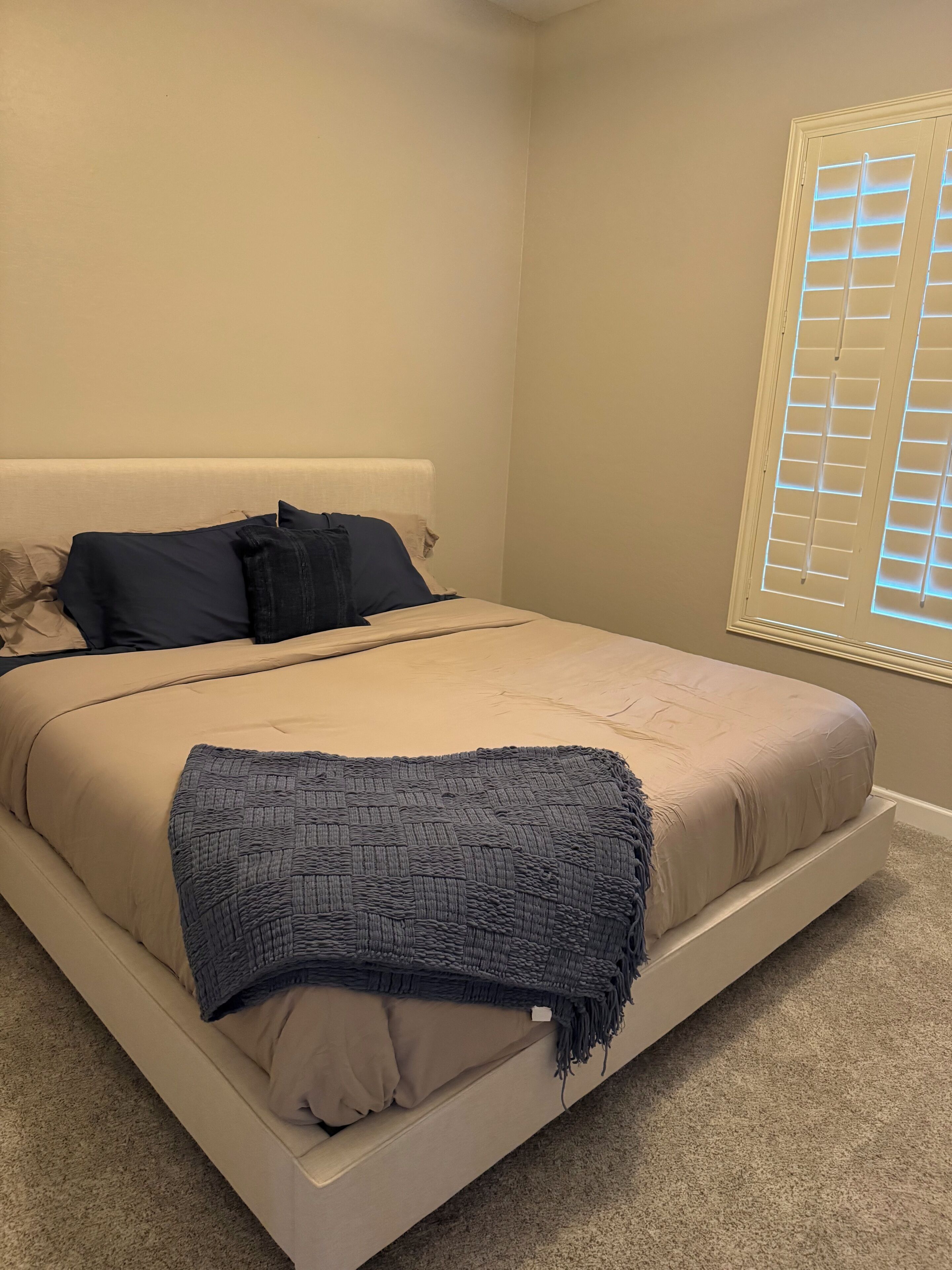 A bedroom with a bed, pillows, a blanket, and a window with blinds.