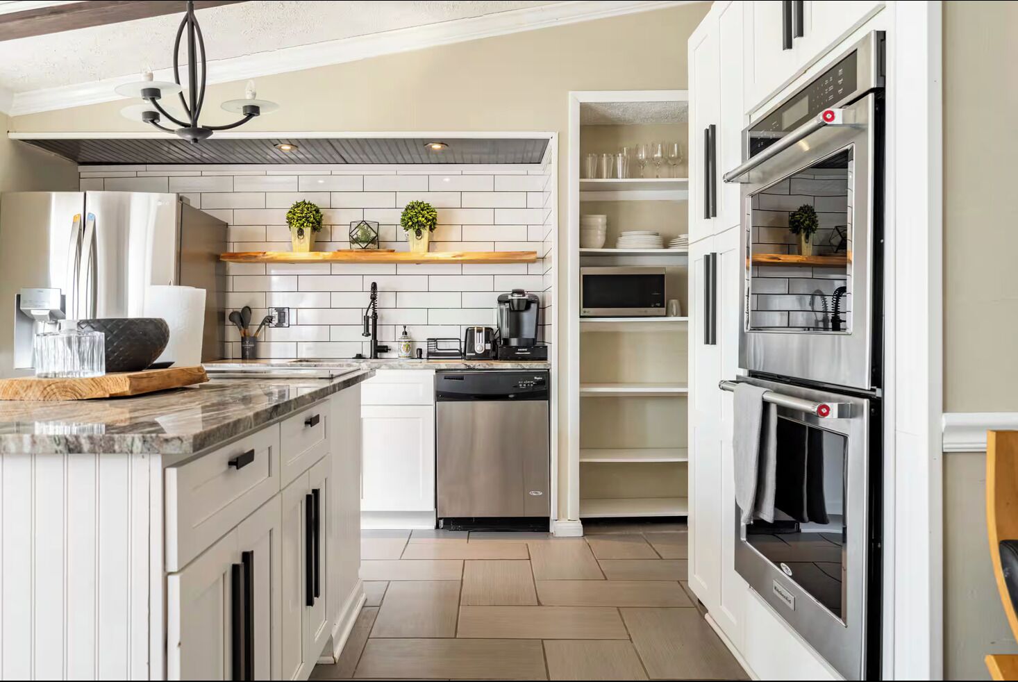 Una cocina moderna con lavavajillas integrado, microondas y horno doble. Cuenta con gabinetes blancos y encimera de mármol.
