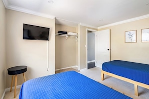 Une chambre avec deux lits, une télévision, un placard et une porte donnant sur une autre pièce.