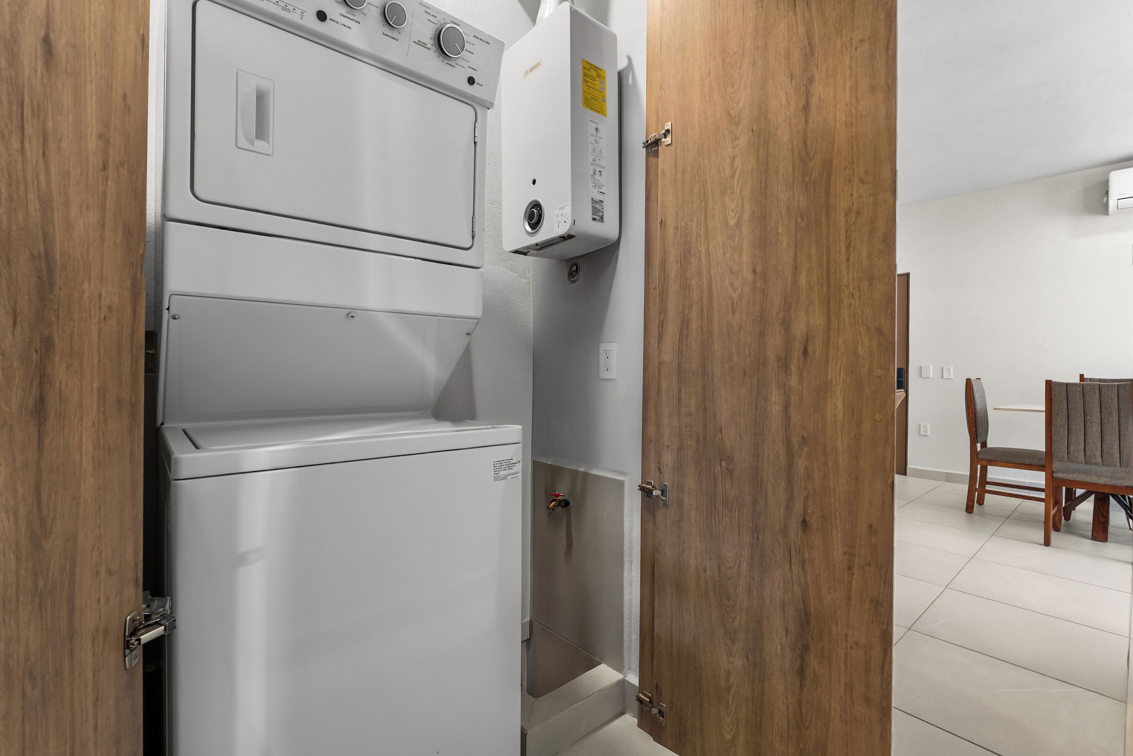 Un lavadero con lavadora y secadora apiladas, puertas de madera y un área de comedor visible a través de un acceso abierto.