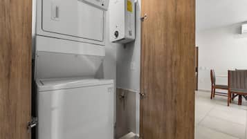 Un lavadero con lavadora y secadora apiladas, puertas de madera y un área de comedor visible a través de un acceso abierto.