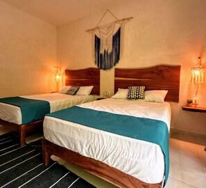 Habitación de hotel con dos camas, cada una con cabecero de madera, ropa de cama blanca y colchas color aguamarina. Hay lámparas de pared a cada lado de las camas.