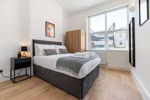 Un dormitorio moderno con cama, mesita de noche y ventana con vista a edificios.