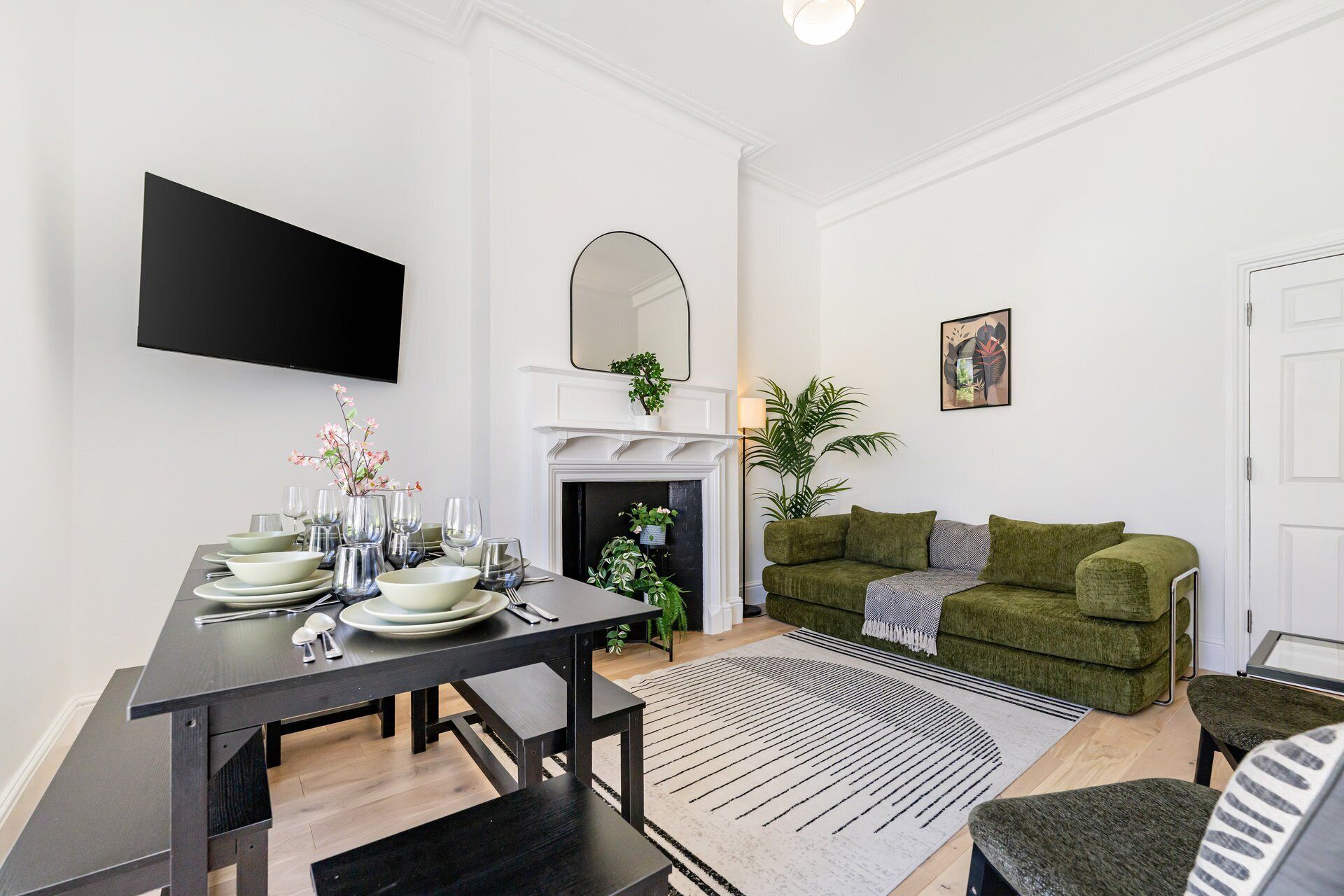 Un salon moderne comprenant un coin repas, une cheminée, un canapé vert et un téléviseur à écran plat fixé au mur.