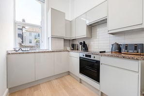 A modern kitchen with white cabinets, a built-in oven, a coffee maker, and a toaster. - Bayswater Two-Bed with Period Charm (London)