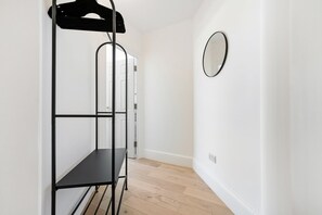 A narrow hallway with a black metal shelf unit, a white door, and a round mirror on the wall. - Bayswater Two-Bed with Period Charm (London)