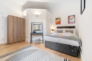 A modern bedroom with a bed, bedside tables, a wardrobe, and artwork on the walls. - Bayswater Two-Bed with Period Charm (London)