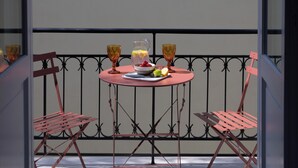 A table with a pitcher, glasses, and fruit on a balcony with metal railings and chairs. - A neoclassical monument with Acropolis view in the Historic Center of Athens (Athina)