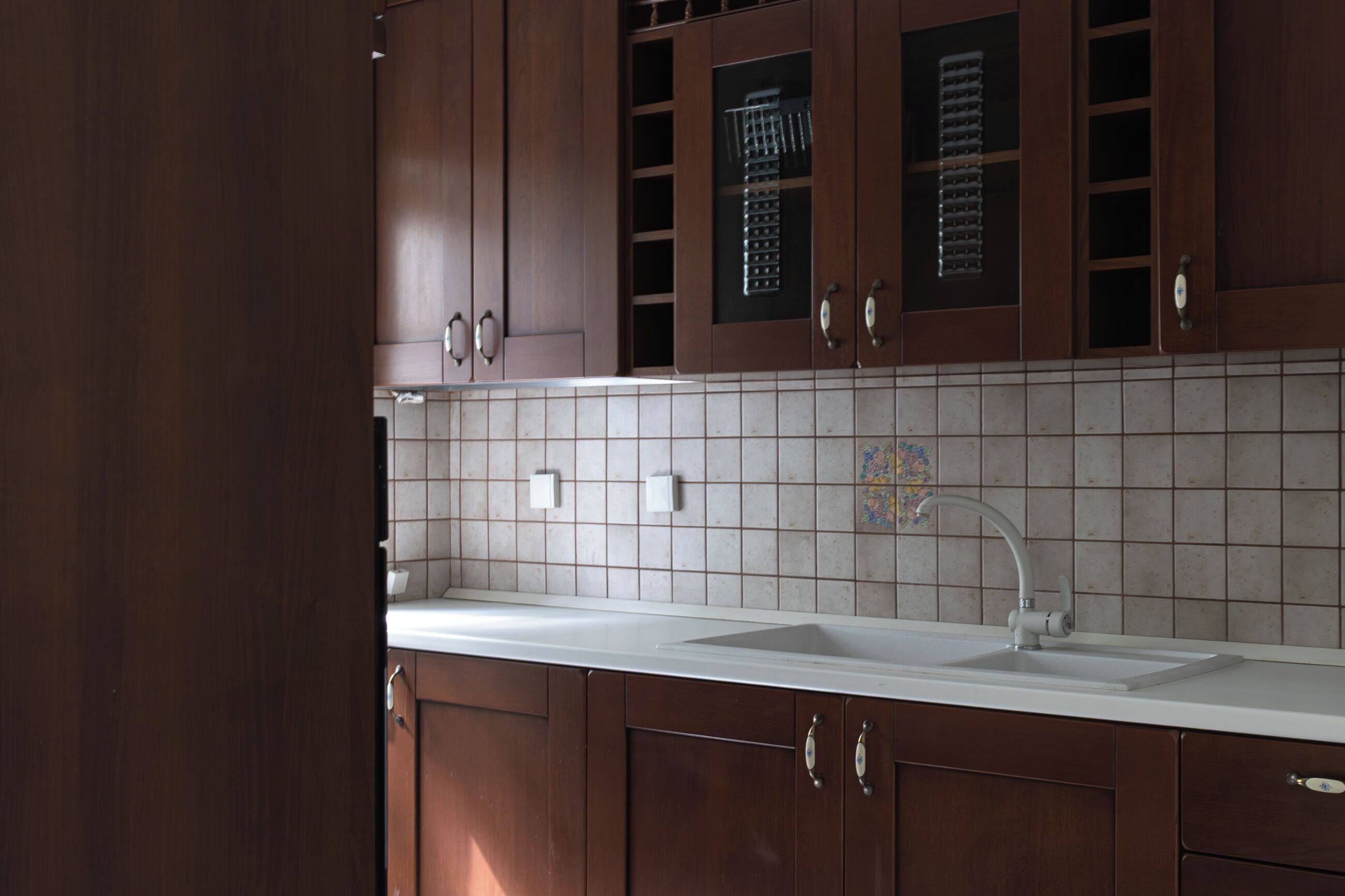 Een keuken met houten kastjes, een wit aanrechtblad en een betegelde spatwand.