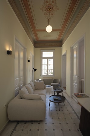 A spacious living room with a large beige sectional sofa, a round coffee table, and a floor lamp. - A neoclassical monument with Acropolis view in the Historic Center of Athens (Athina)