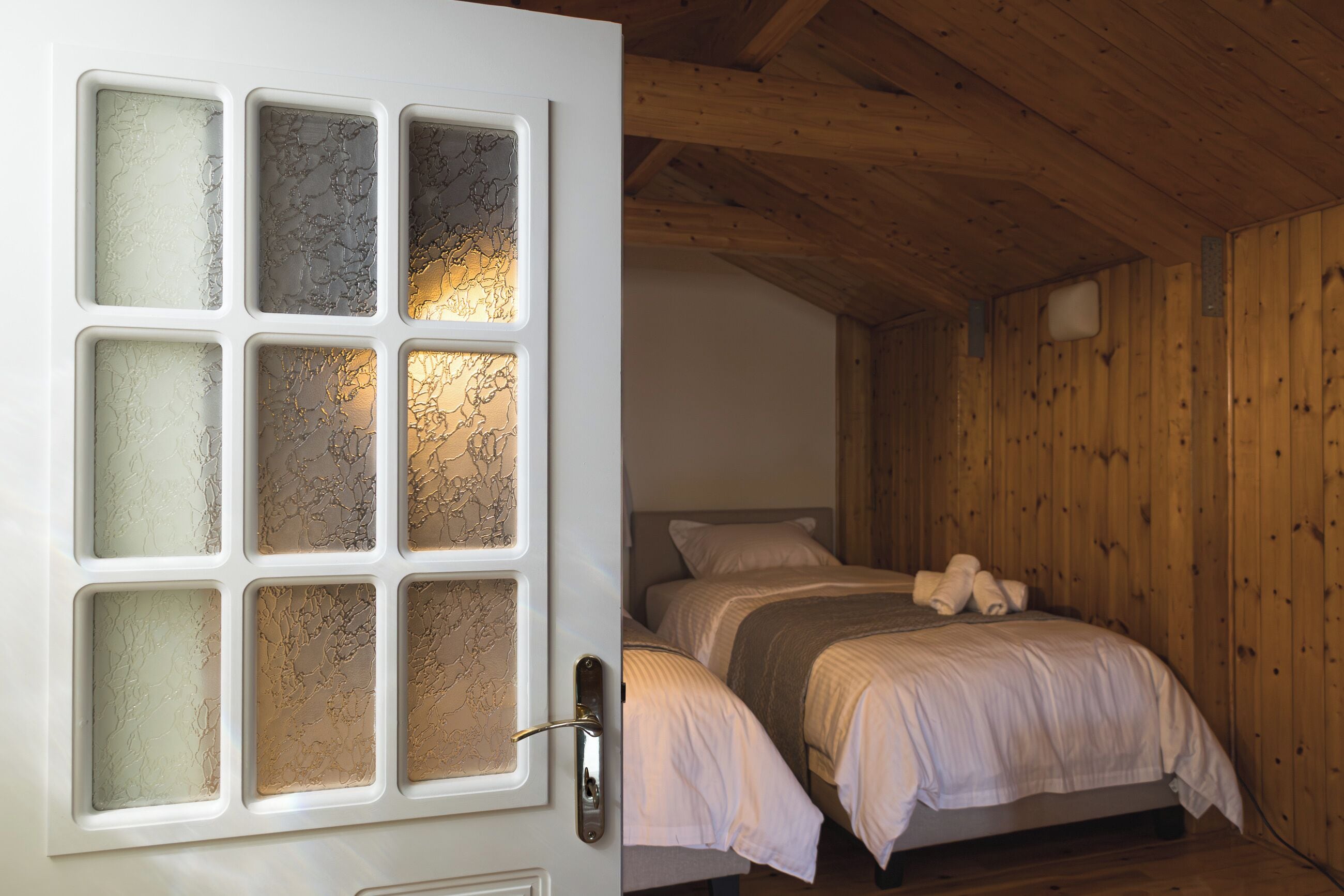 A room with a bed, wooden walls, and a door with frosted glass panels.