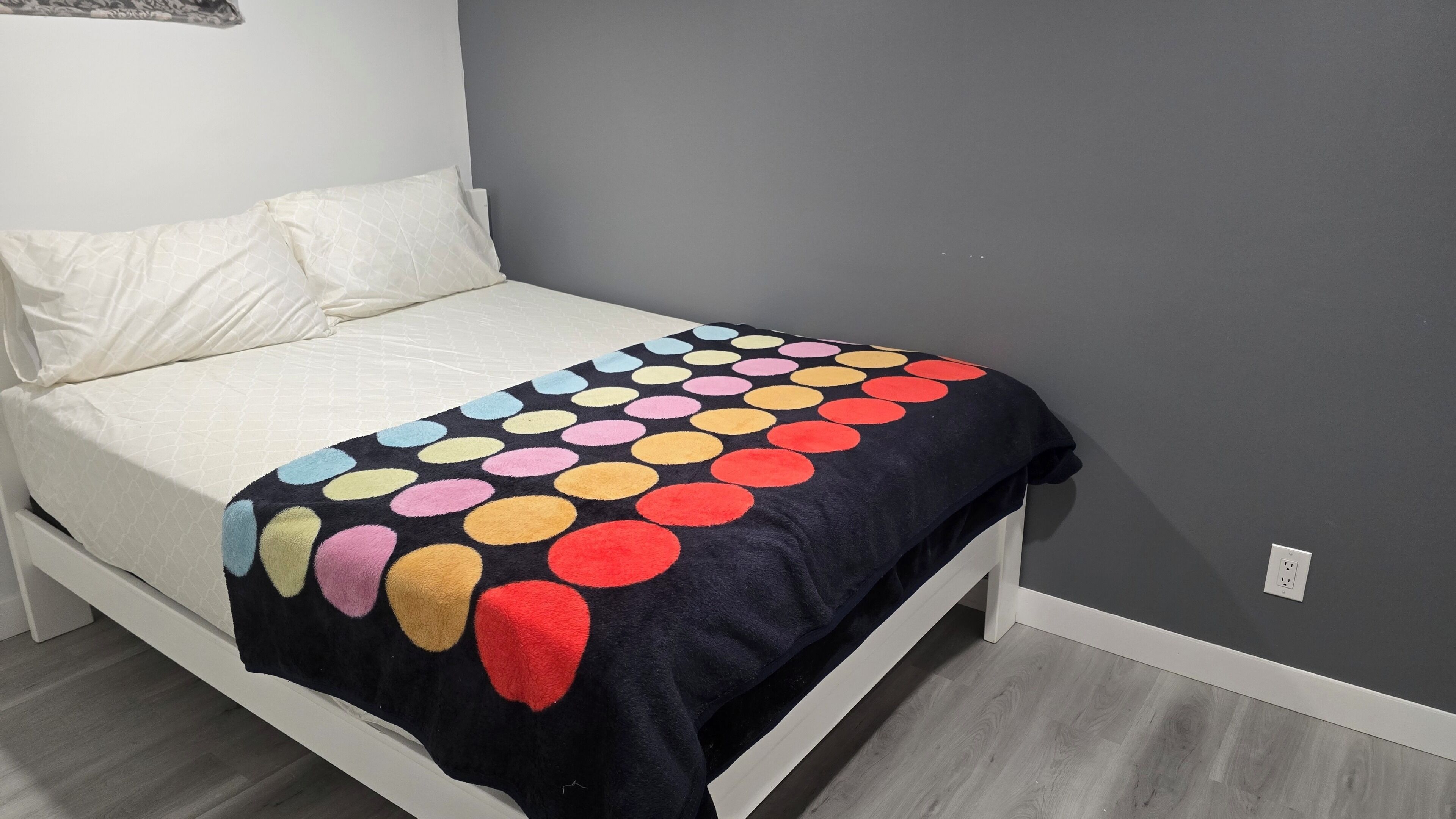 Un llit amb matalàs blanc i manta negra amb dibuixos circulars multicolors.
