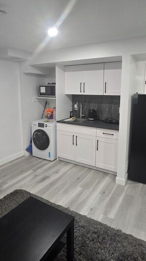 Una cucina compatta con mobili bianchi, un forno a microonde, una macchina da caffè e una lavatrice.
