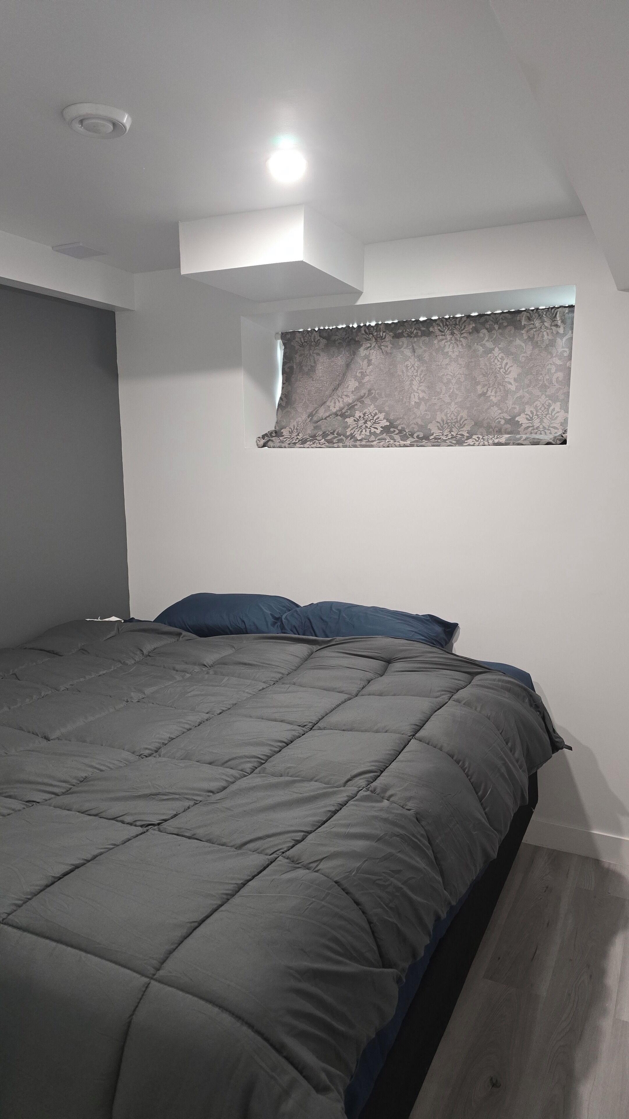 A bedroom with a bed, a window with curtains, and a ceiling light.