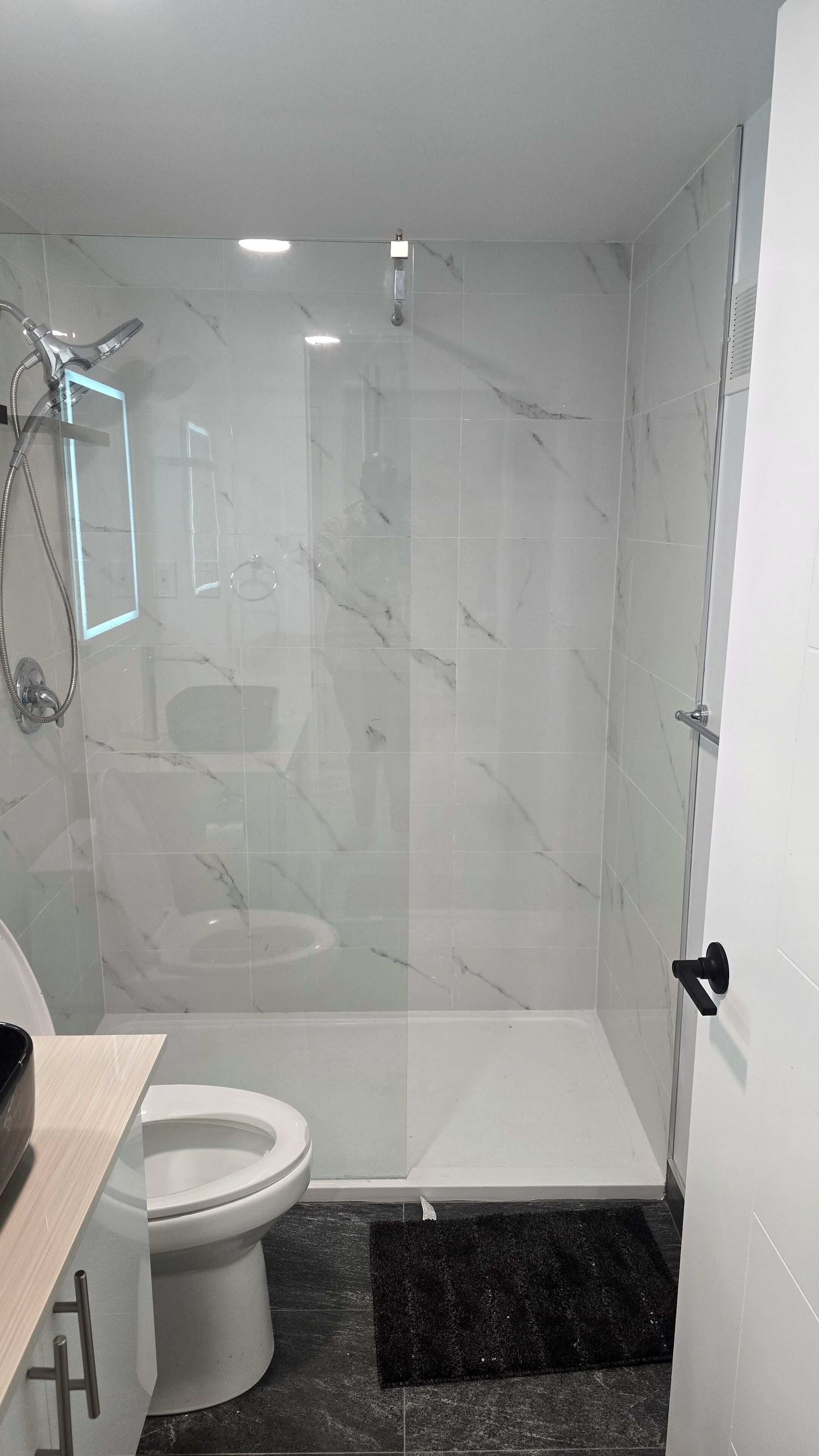 A modern bathroom with a glass-enclosed shower, a white toilet, and a marble-tiled shower wall.