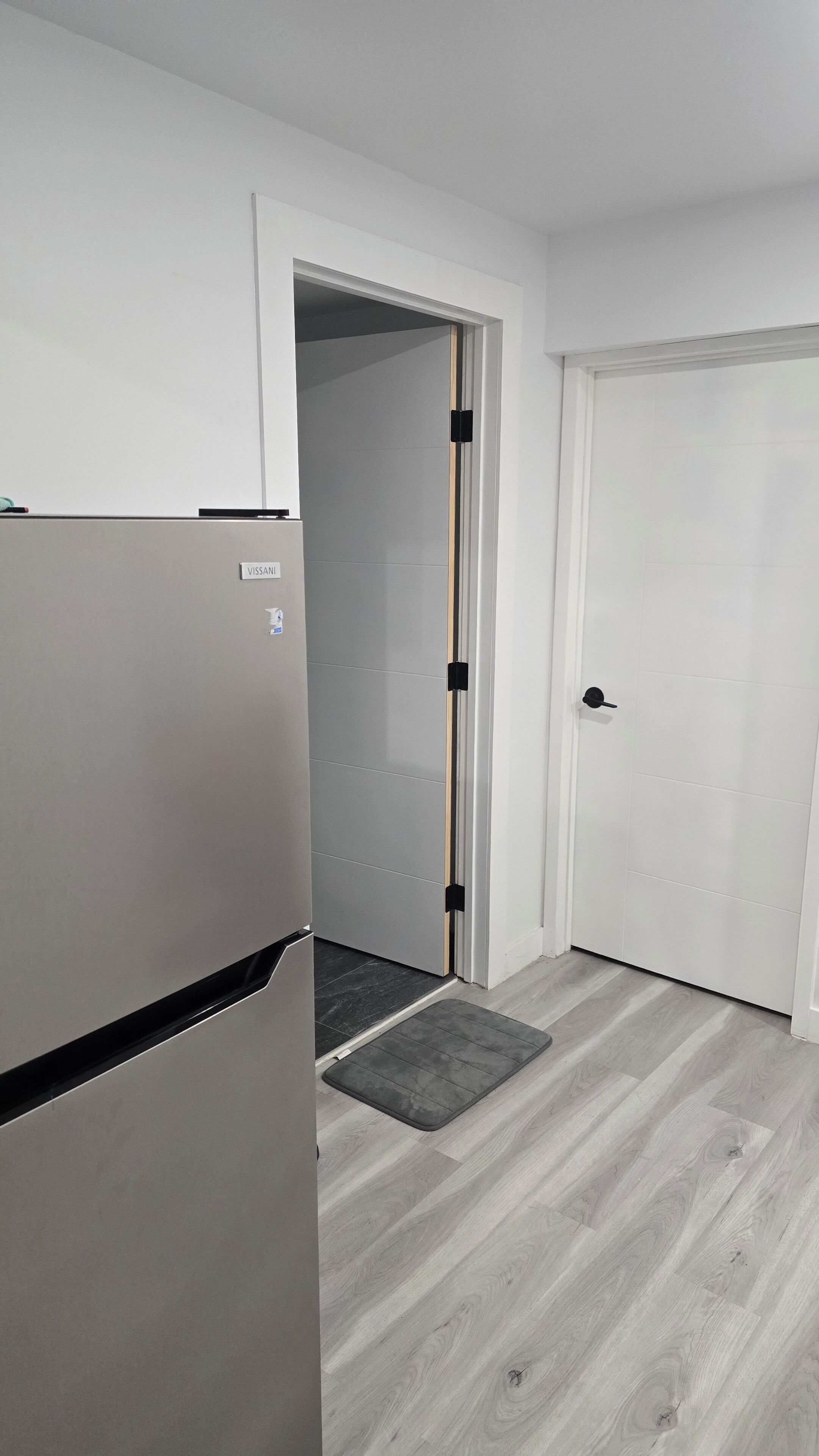 A room with a white door, a white wall, and a grey floor.