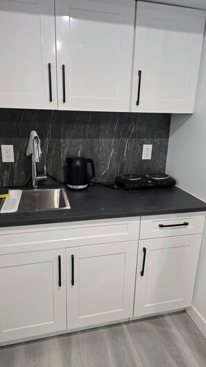 Una cucina moderna con mobili bianchi, un piano di lavoro nero, un lavello in acciaio inossidabile, una macchina da caffè nera e un piano cottura elettrico compatto.