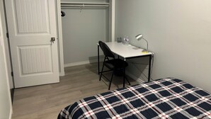 A room with a bed, a desk with a chair, a desk lamp, and a water bottle. There is a door with a sign indicating 'Room No.2'.