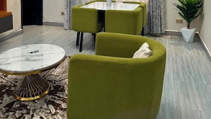 Ett modernt vardagsrum med en matplats, med ett runt soffbord, gröna fåtöljer och ett matbord med glasskiva.
