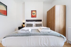 A hotel room with a bed, a nightstand, a wall art piece, and a wardrobe. - Elegant Bayswater Two-Bed near Hyde Park (London)