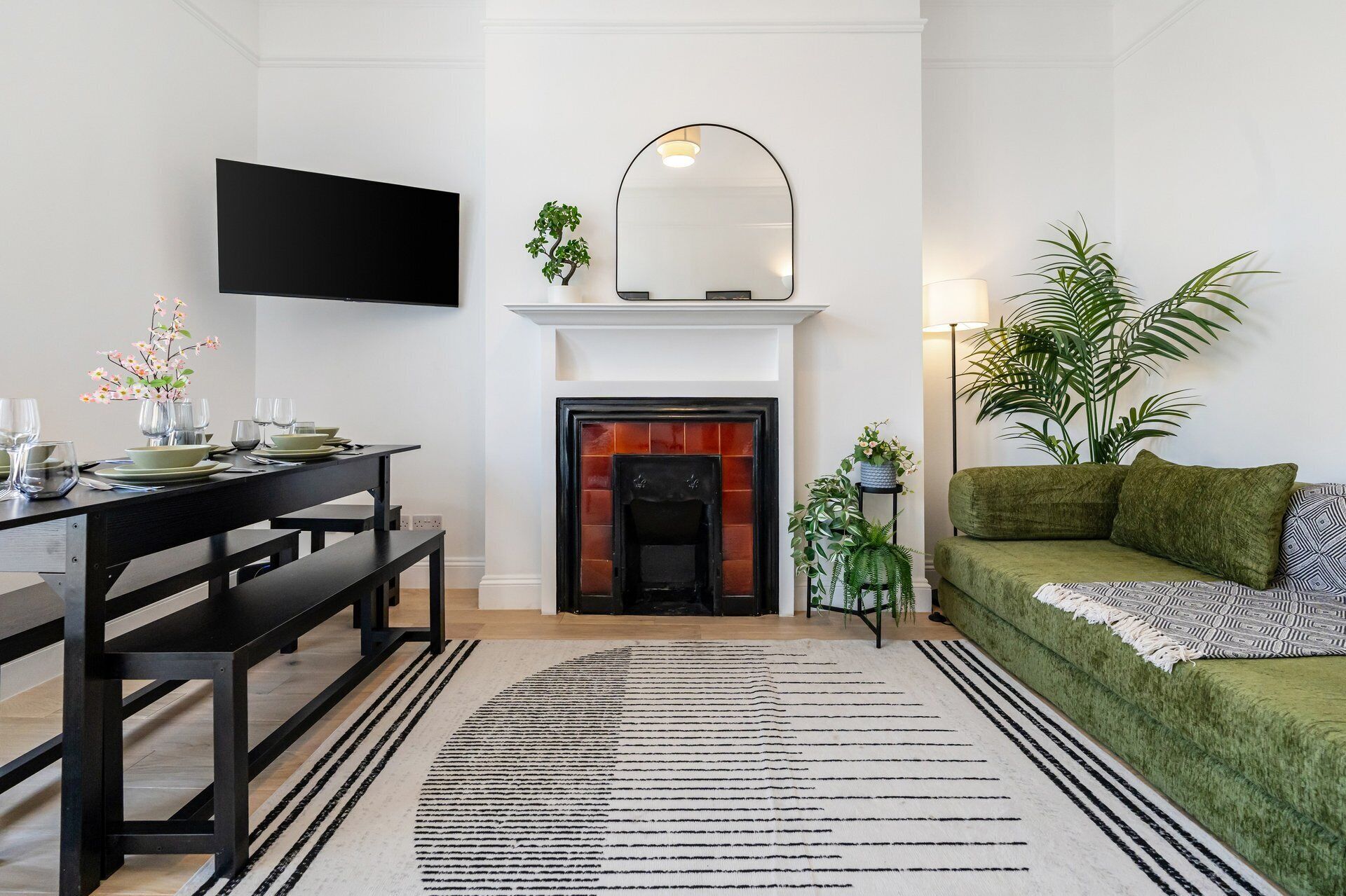 A modern living room with a fireplace, a flat-screen TV mounted above it, a green sofa, and a dining area with a table set for four.