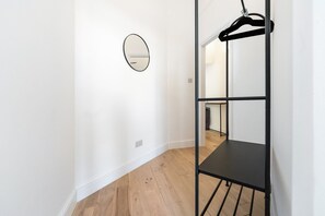 A room with a black metal shelf unit, a round mirror on the wall, and a wooden floor. - Elegant Bayswater Two-Bed near Hyde Park (London)