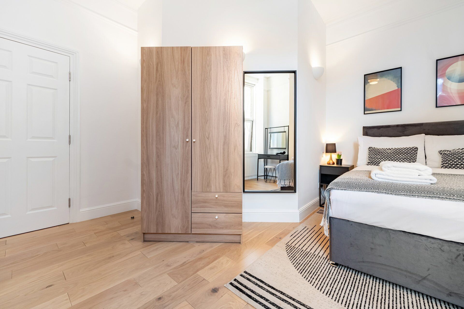Une chambre moderne avec un grand lit, une armoire, un bureau avec une chaise et un miroir.