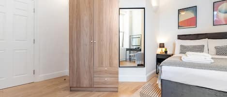 A modern bedroom with a large bed, a wardrobe, a desk with a chair, and a mirror.