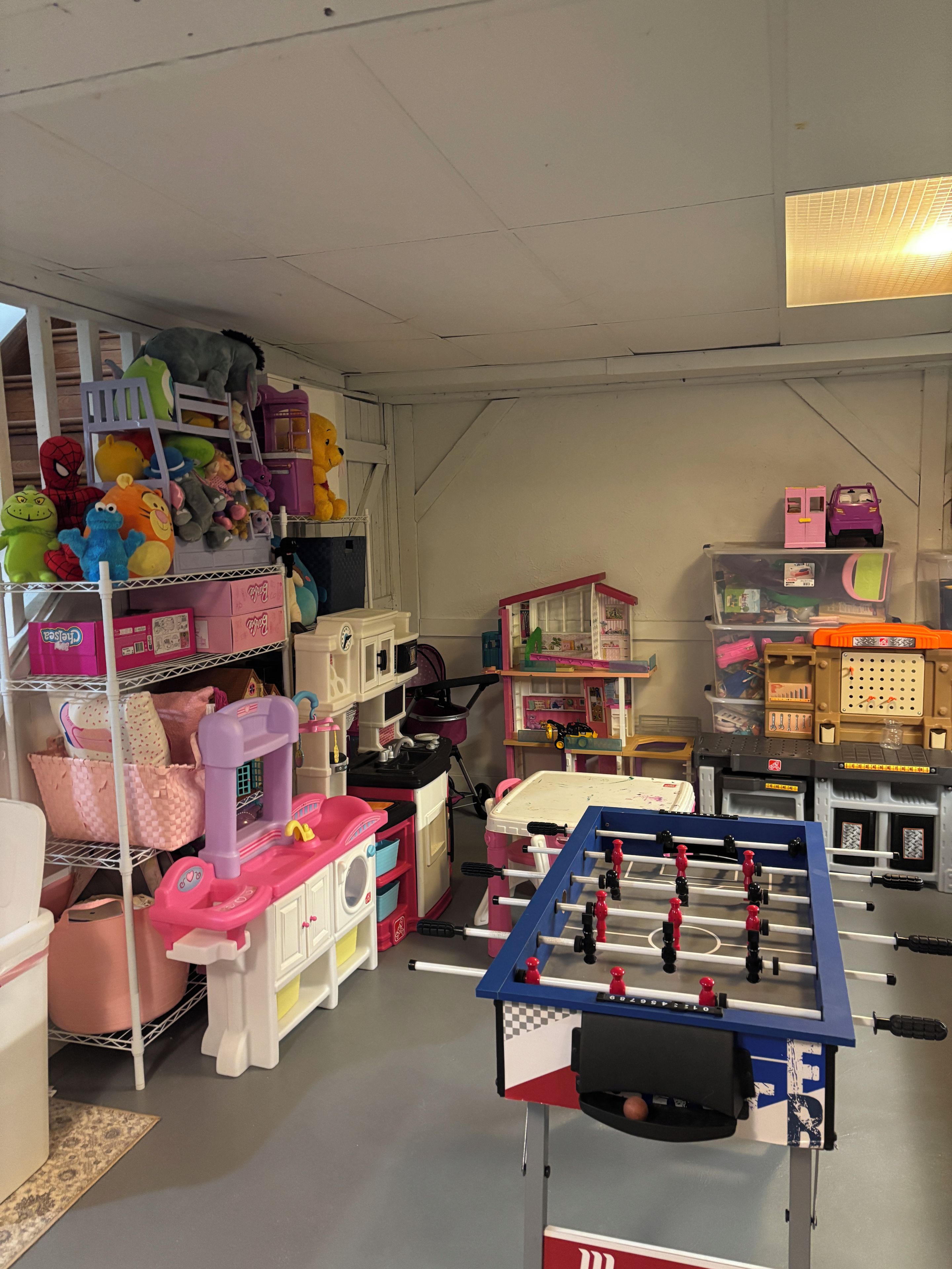 A room with a foosball table, shelves with stuffed toys, and various storage bins.